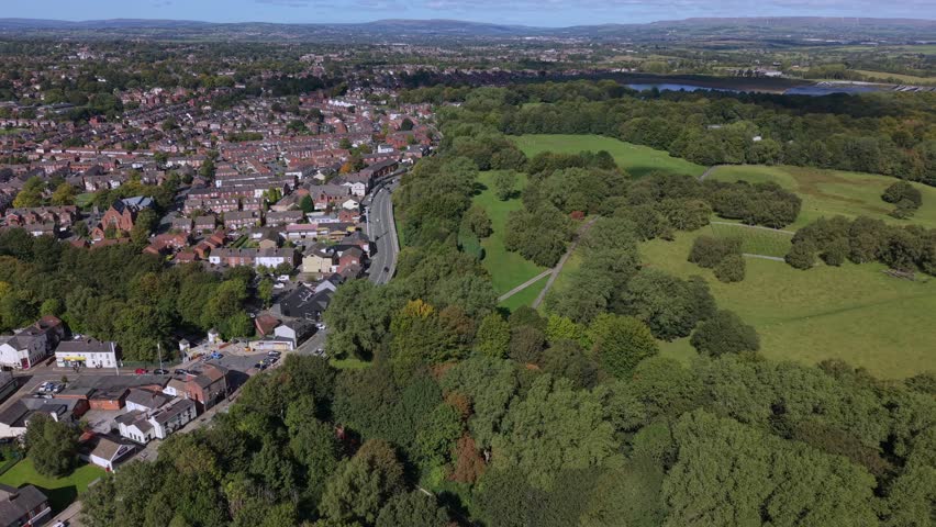 Aerial video of Heaton Park fields, woodland, and suburban Prestwich housing under a clear blue sky. Manchester - UK. 