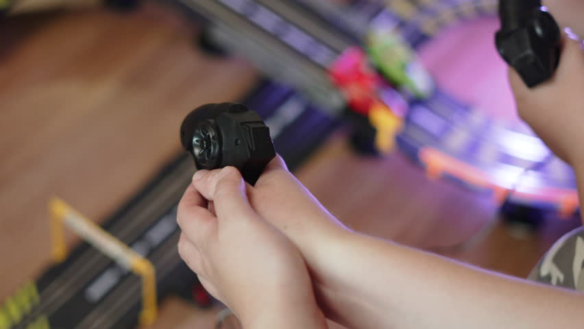 Two teenagers play racing game using joysticks, viewed from above. Unrecognizable young people move toy cars around blurred track with controllers. Offline, non-digital, physical game.