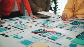 Team members engage in a collaborative design session, creating wireframes and smartphone prototypes on a sleek table, fostering innovation and creativity in user interface development. SACTR - Powered by Shutterstock - Get 15% off with code: PIKWIZARD15