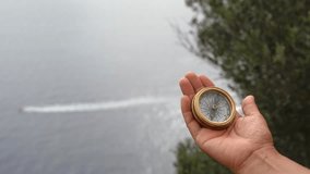 Vintage brass compass held in someone's hand, with a serene lake and a boat racing past in the background. Evoking themes of exploration, orienteering, and journeying through unfamiliar territories - Powered by Shutterstock - Get 15% off with code: PIKWIZARD15