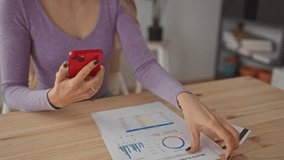 Woman holding smartphone and document in living room while analyzing data, surrounded by credit card and paperwork on wooden table, suggesting financial planning at home. - Powered by Shutterstock - Get 15% off with code: PIKWIZARD15