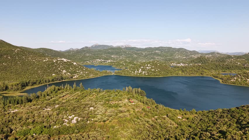 Panoramic aerial view of the serene Bacina Lakes in Croatia, a stunning natural landscape featuring interconnected freshwater lakes surrounded by lush green hills and a clear blue sky, travel themes