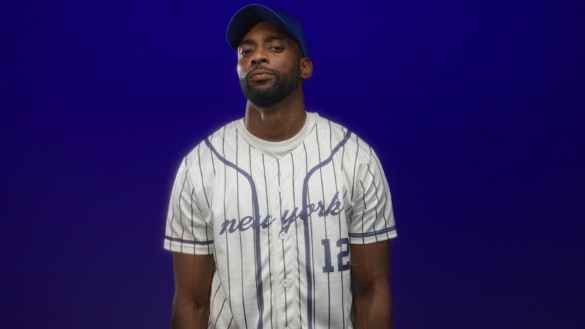 Man baseball player with crossed arms in studio against deep blue backdrop; confidence determination.