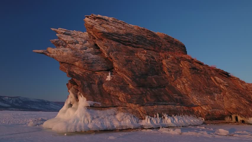 Aerial around Ogoy Rock on frozen Lake Baikal, Siberia. Best winter tourist destination with scenic pancake ice patterns and icicles at epic golden hour. Vast snowy landscape. Travel landmark Buryatia