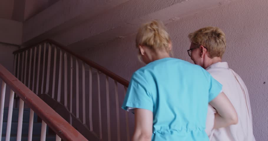 Caregiver nurse assists elderly senior on stairs. In a staircase, the aide offers guidance and assistance, helping ensure safety while ascending with care. Caring support and nursing e service.
