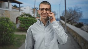 Man smiling while talking on smartphone outdoors in sunny street near ocean showcasing relaxed lifestyle and communication in coastal urban environment. - Powered by Shutterstock - Get 15% off with code: PIKWIZARD15