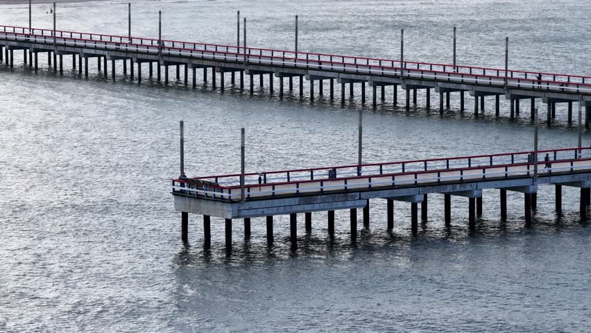Close-up view of a wooden pier with red and blue railings stretching into the Baltic Sea in Palanga, Lithuania, with people walking along the structure.