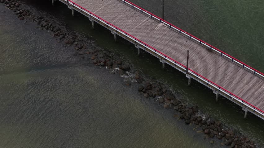 Close-up view of a wooden pier with red and blue railings stretching into the Baltic Sea in Palanga, Lithuania, with people walking along the structure.