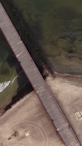 Close-up view of a wooden pier with red and blue railings stretching into the Baltic Sea in Palanga, Lithuania, with people walking along the structure.