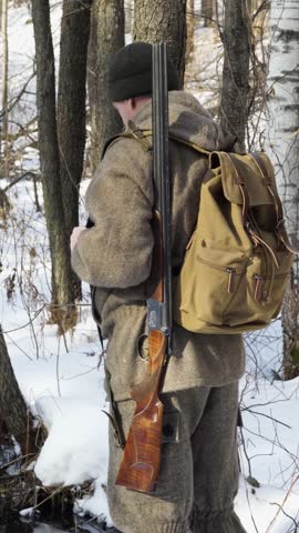 A lone hunter with a gun in a winter forest. Rear view. Tracking and hunting wild forest animals. Vertical video.