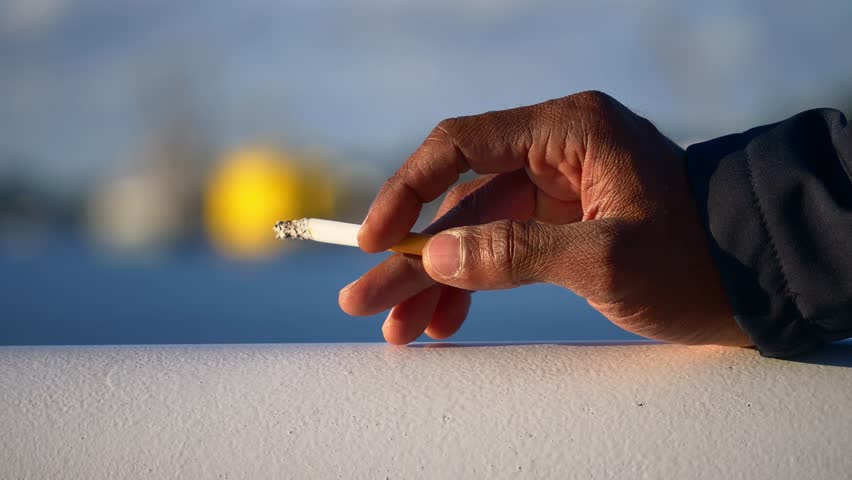 Hand with holding a lit cigarette while waiting calmly, smoking, blurred and colorful background.