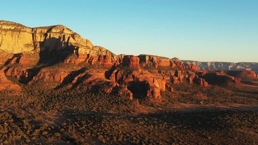 Aerial drone footage of Bear Mountain and red rock formations at sunset in Sedona, Arizona, with warm golden light and slow dolly-in camera motion over the dramatic desert landscape.