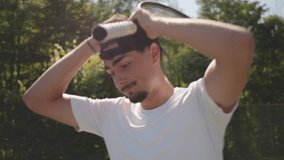 Close-up of a young man in a white shirt practicing tennis on a hardcourt, adjusting his headband. Outdoor setting with lush greenery highlights focus and dedication in sports training. - Powered by Shutterstock - Get 15% off with code: PIKWIZARD15