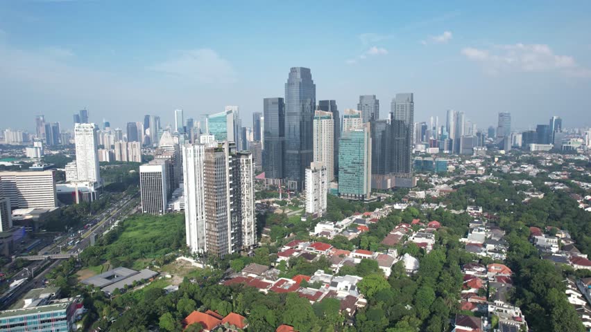 Aerial view of Jakarta skyline with modern skyscrapers and green residential areas, highlighting the contrast between urban development and traditional housing.