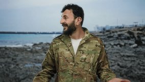 Hispanic man with beard in military uniform standing on rocky beach with sea backdrop, looking confident and expressive, blending military presence with tranquil coastal scenery. - Powered by Shutterstock - Get 15% off with code: PIKWIZARD15