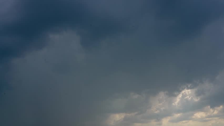 Dark, heavy rain clouds fill the sky during daylight hours. Rain falls as the ominous sky moves across the land