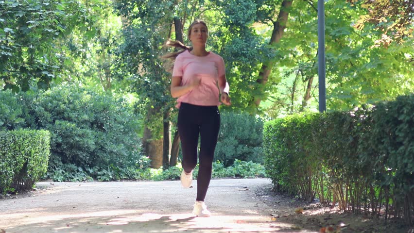 Young athletic woman experiencing a sudden leg muscle cramp and intense pain while running in the park, forcing her to stop her workout and massage the sore area to relieve the discomfort