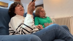 Senior women friends sitting on a sofa at home watching television together and relaxing with drinks - Powered by Shutterstock - Get 15% off with code: PIKWIZARD15