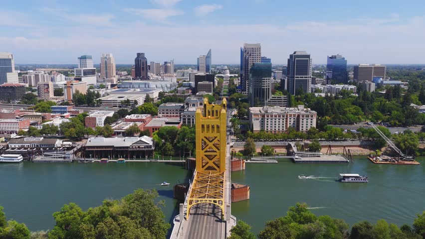 Aerial view of Sacramento, California, featuring the yellow Tower Bridge, downtown skyline, capitol building, and boats moving on the Sacramento River.