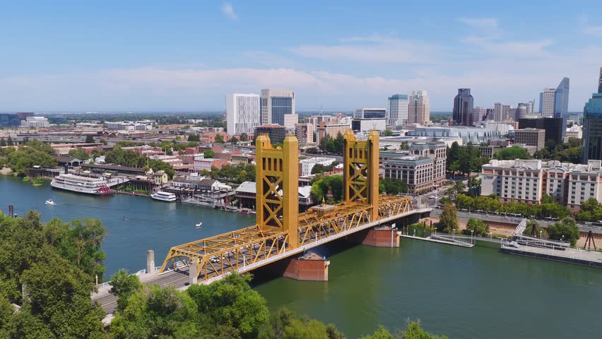 Aerial view of Sacramento, California, featuring the golden Tower Bridge, calm Sacramento River, city skyline, and California State Capitol dome.