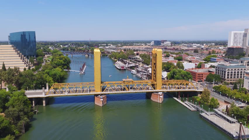 Aerial view of Sacramento, California, featuring the golden Tower Bridge, Sacramento River, downtown skyline, and boats along the riverbank.