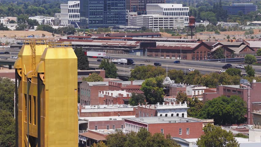 Aerial view of Sacramento, California, showing the Tower Bridge, urban buildings, tree lined streets, and moving highway traffic.