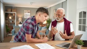 Caring grandson helping his senior grandfather with paperwork, explaining how to use a laptop and fill out documents. Two generations interacting, sharing knowledge, and bonding at home - Powered by Shutterstock - Get 15% off with code: PIKWIZARD15