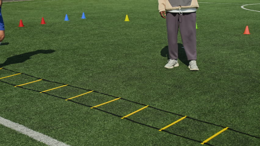 Slow motion of three preteen football players exercising on agility ladder while his African American coach standing and watching