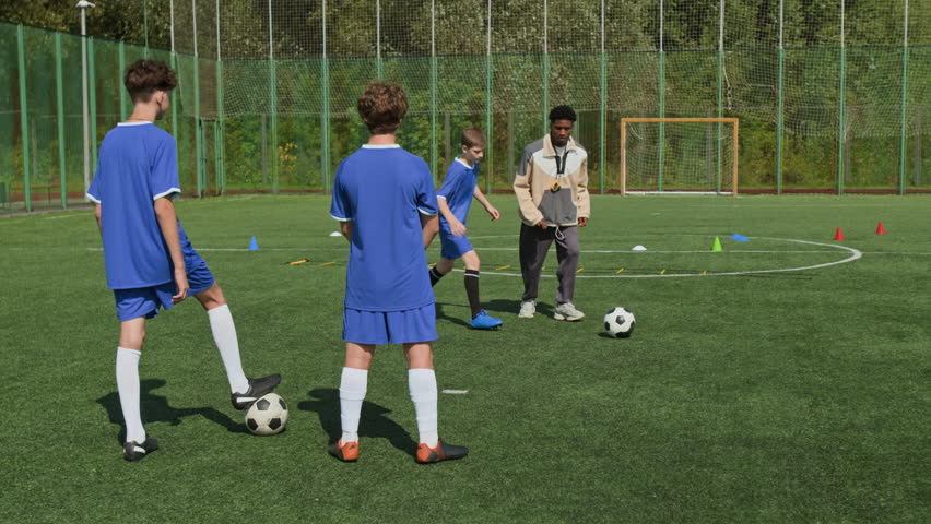 African American coach showing block exercise and kicking football to two boys