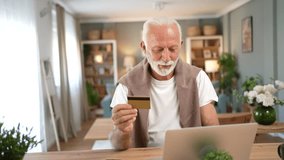 Happy senior man with a white beard sitting at home, holding a credit card and making an online payment on his laptop, smiling while enjoying the convenience of electronic banking - Powered by Shutterstock - Get 15% off with code: PIKWIZARD15