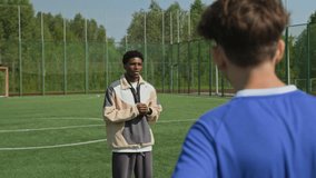 Back view shot of three football players standing on pitch, looking at African American coach explaining game strategy - Powered by Shutterstock - Get 15% off with code: PIKWIZARD15
