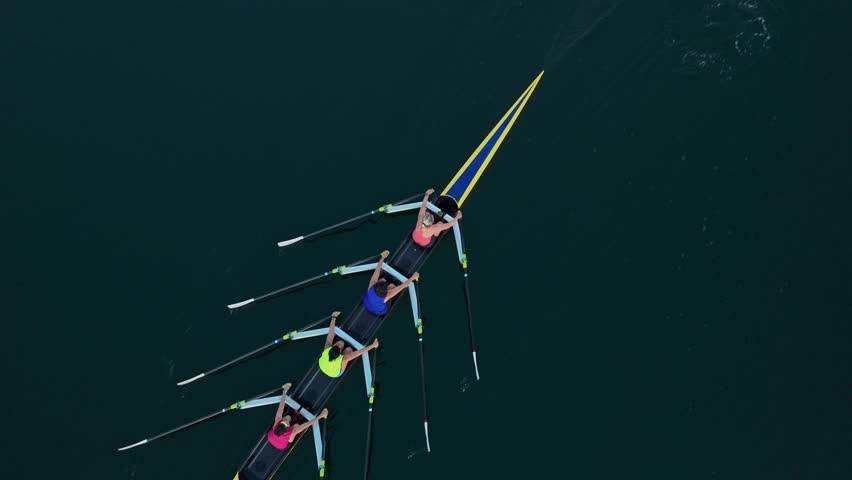 Aerial view Beautiful Sunrise Light Reflects On Ocean As A Rowing Boat With Four Female Athletes Glides Smoothly, Captured From Above During An Early Morning Practice In Summer.