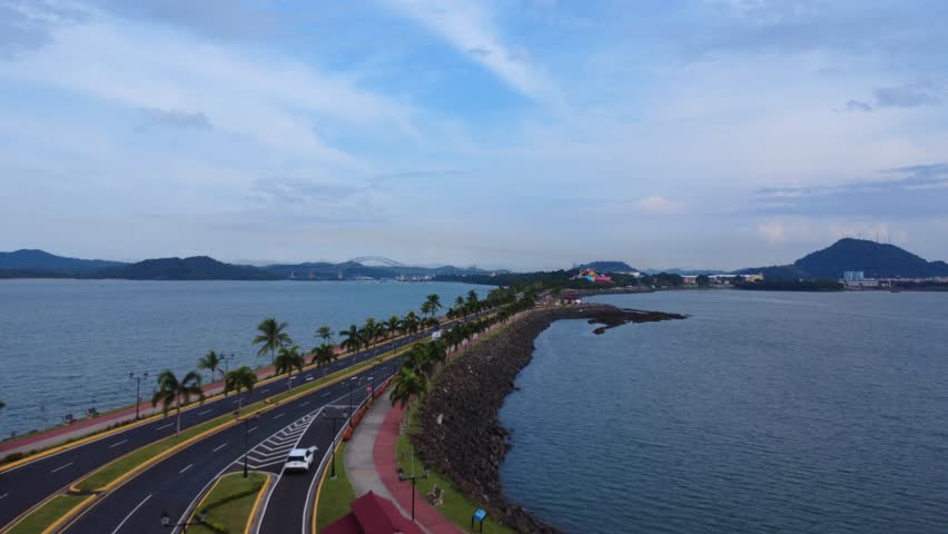 Coastal highway with palm trees and ocean views leading to distant bridges and hills