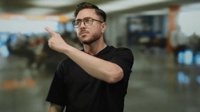 Young man with beard pointing indoors at busy airport terminal indicating directions for travelers seeking assistance or wayfinding - Powered by Shutterstock - Get 15% off with code: PIKWIZARD15