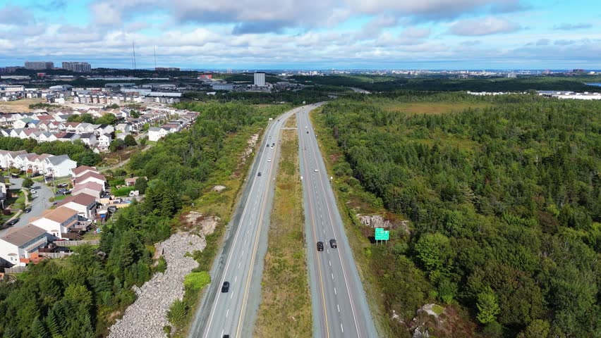 Aerial view Long Lanes Filled With Vehicles In Motion, Scenic Forests On Both Sides, And A Sunlit Roadway Capturing Canadian Commute From Above. Nova Scotia, Halifax, Canada.