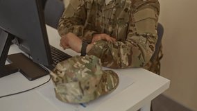 Hispanic soldier in camouflage uniform adjusting his glasses at office computer desk beside a keyboard and monitor; determination resilience focus confidence. - Powered by Shutterstock - Get 15% off with code: PIKWIZARD15