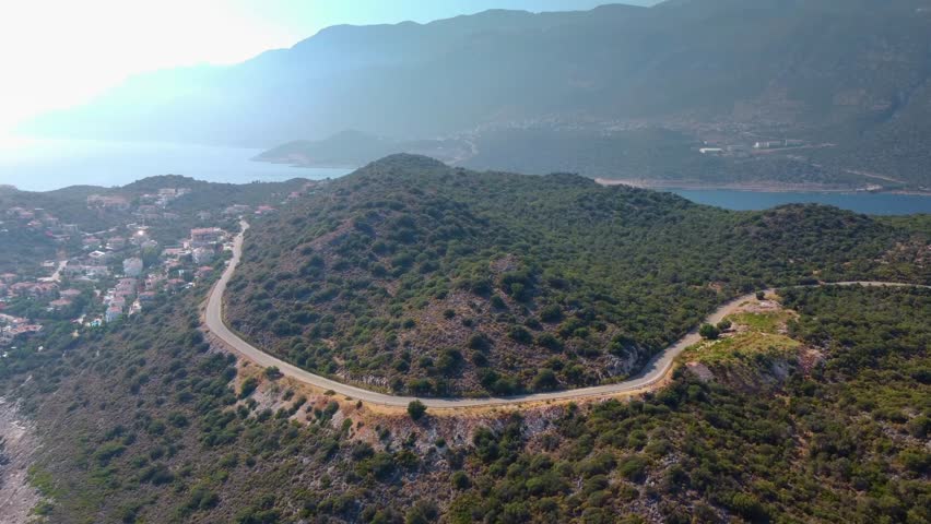 Drone footage capturing the coastal road and vibrant Mediterranean landscape near Kas, Antalya, Turkey. Featuring winding roads, lush green hills, and the sparkling turquoise sea, perfect for travel,