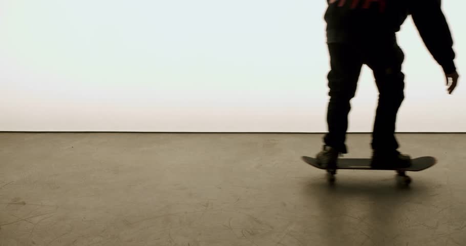 A young skater picks up their skateboard in a minimal studio setting. The bright background and simple environment create a clean look. This is great footage for extreme sports, skateboarding culture,