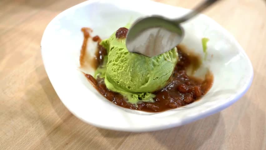 Spoon scoops matcha ice cream. Green tea dessert served in white bowl with sweet red bean paste. Sweet food concept. background food and healthy lifestyle content