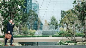 Side view of businessman calling manager about marketing report and walking at modern building in green eco city. Leader going to workplace while talking to his team by using phone. Lifestyle. Urbane. - Powered by Shutterstock - Get 15% off with code: PIKWIZARD15