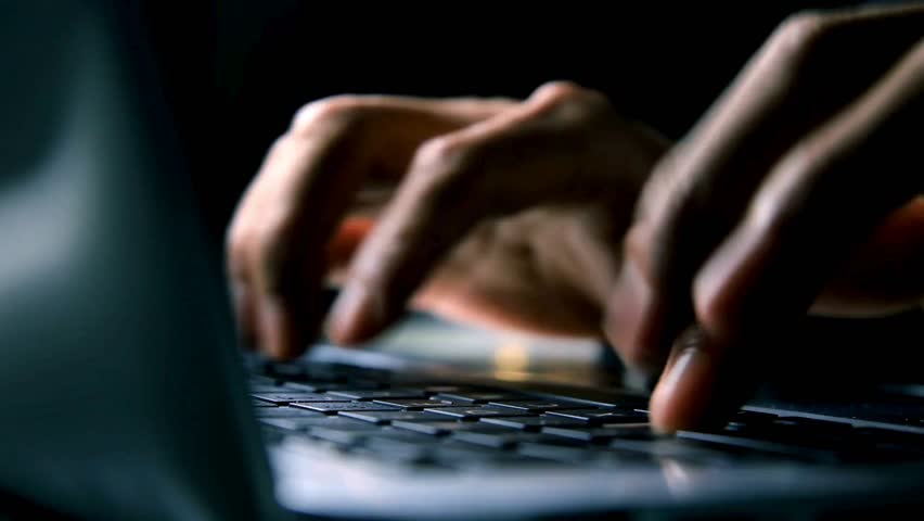Hands quickly type on laptop keyboard under dim light. Person works intently, possibly coding or writing late at night on illuminated computer.