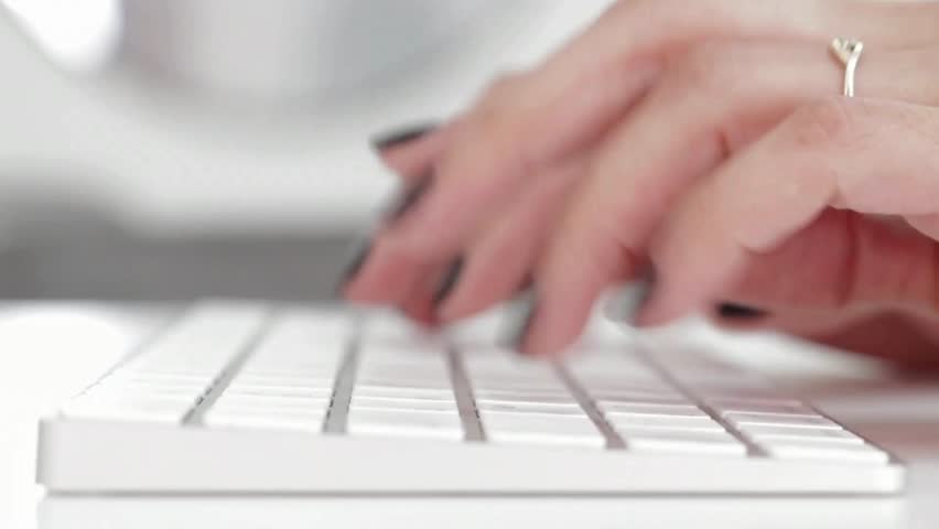 Close-up view of hands with black nails quickly typing on a sleek keyboard, emphasizing productivity and digital engagement in a bright workspace.