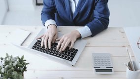 Businesswoman typing On Laptop. Hands type on laptop keyboard. Woman in blue jacket works at bright wooden desk with calculator, plant, and pencils on it. Top view. - Powered by Shutterstock - Get 15% off with code: PIKWIZARD15