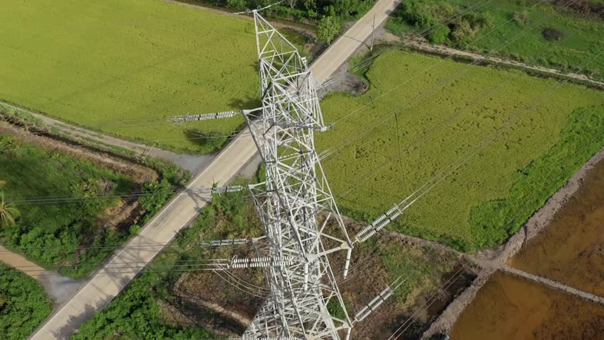 Power transmission lines Pylon towers rise above vibrant green fields, showcasing electricity infrastructure in a serene rural setting under clear sky.