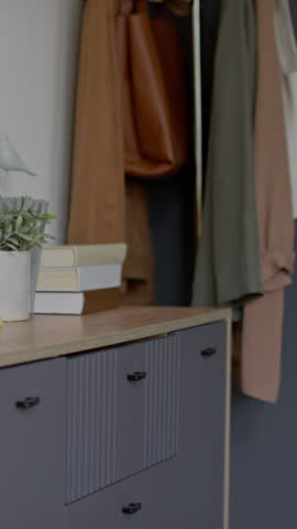 Medium vertical shot of anonymous young woman wearing pajama shorts opening dresser drawer and taking out folded casual clothes while getting ready to go to work in morning