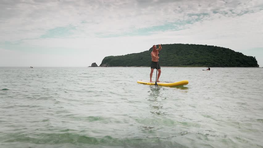 Strong man stands on paddleboard with determined look while navigating sea. Concept of inner strength, masculinity, solo travel, and mindful connection with water and freedom.