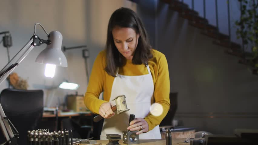 Female craftsperson hammering metal component for tech demo as animated network icons expanding. Craftsman, workshop, craftsmanship, industrial, creative, innovation, construction