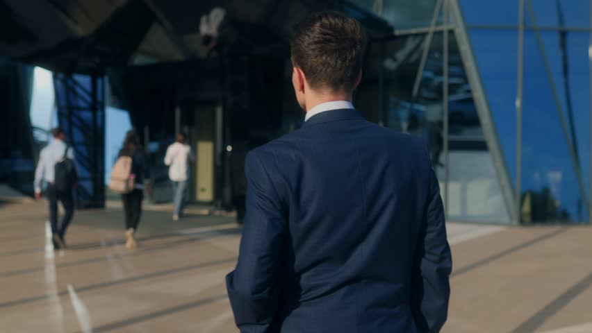A stylish young professional in a suit walks down a city street, exuding determination and ambition, with tall glass buildings highlighting the modern lifestyle.