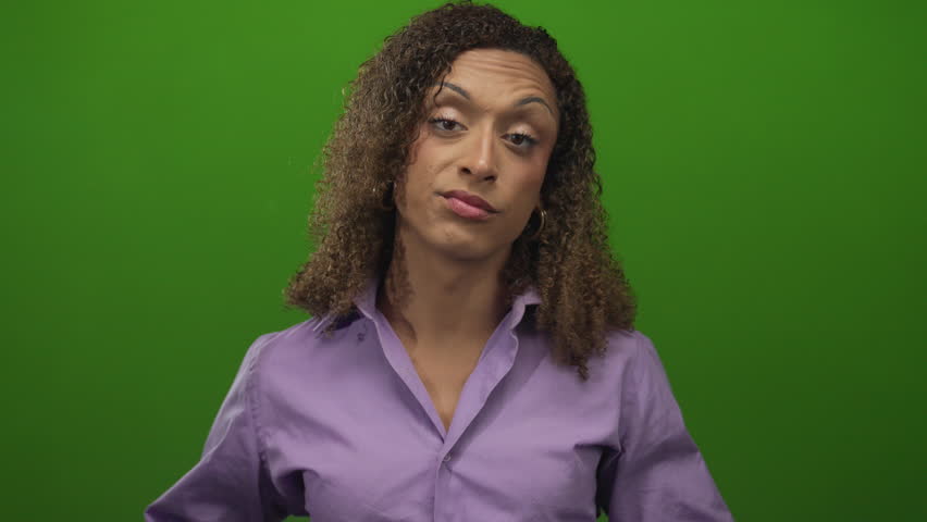 Woman wearing purple shirt makes air quotes gesture with curled fingers and raised eyebrows in studio under green lighting; skepticism.