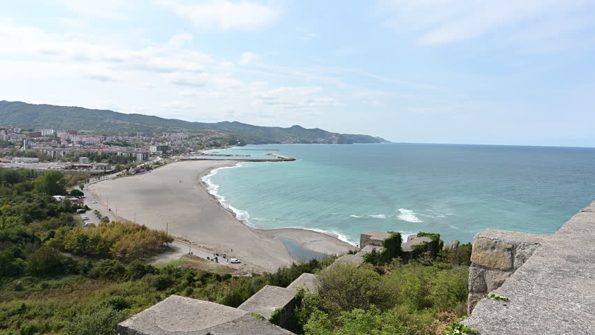 A high viewpoint frames a sandy bay, turquoise shoreline, and densely built coastal town extending toward distant hills.